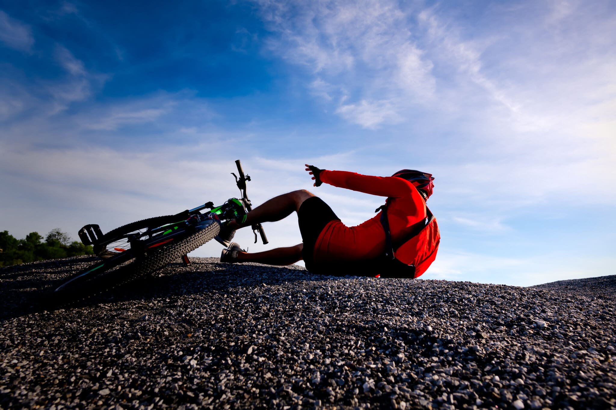 A man in red shirt on ground with bicycle.