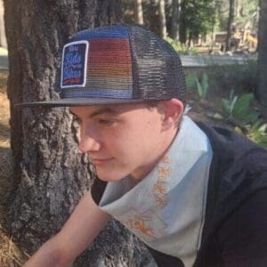Man wearing cap sitting by a tree.