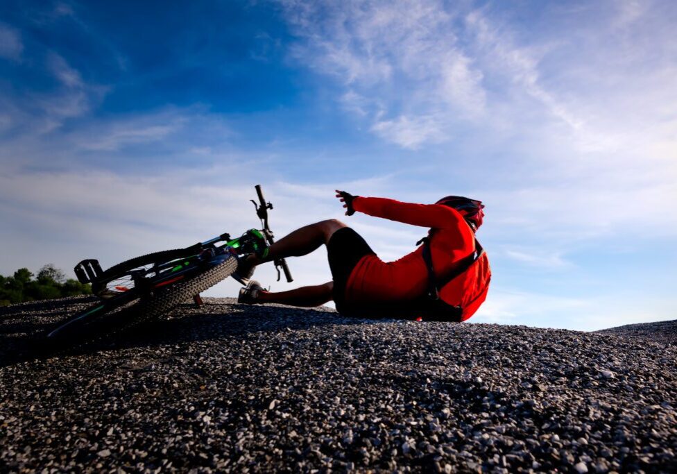 A man in red shirt on ground with bicycle.